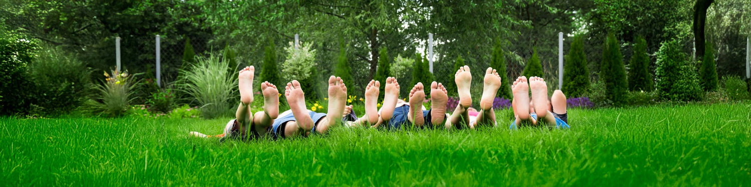 Kids supportive footwear displayed with children lying on grass, showcasing happy feet and comfortable footwear.