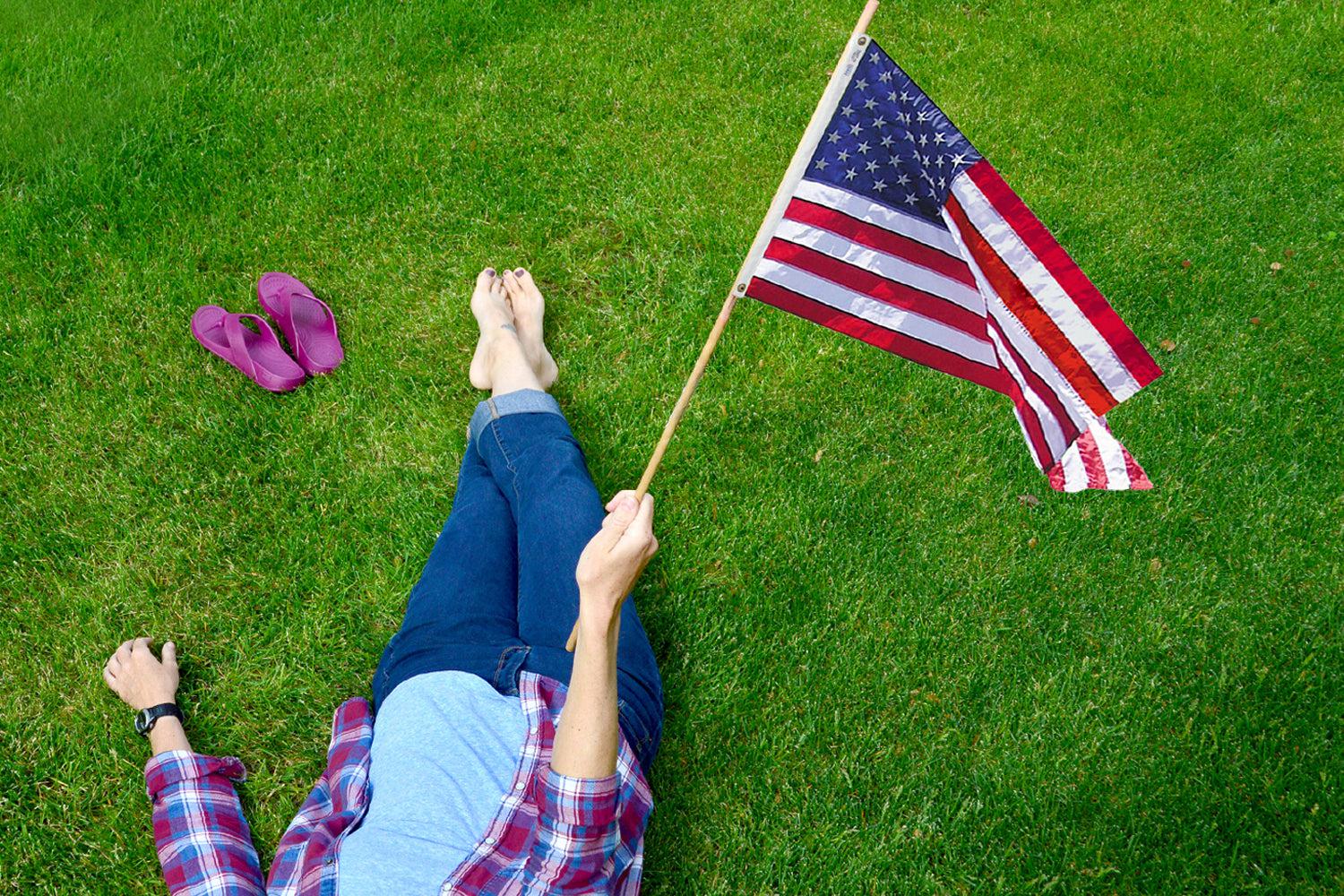NuuSol-Girl laying in grass with a pair of Rustic Wine flip flops lying next to her. She's holding an American flag.