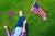NuuSol-Girl laying in grass with a pair of Rustic Wine flip flops lying next to her. She's holding an American flag.